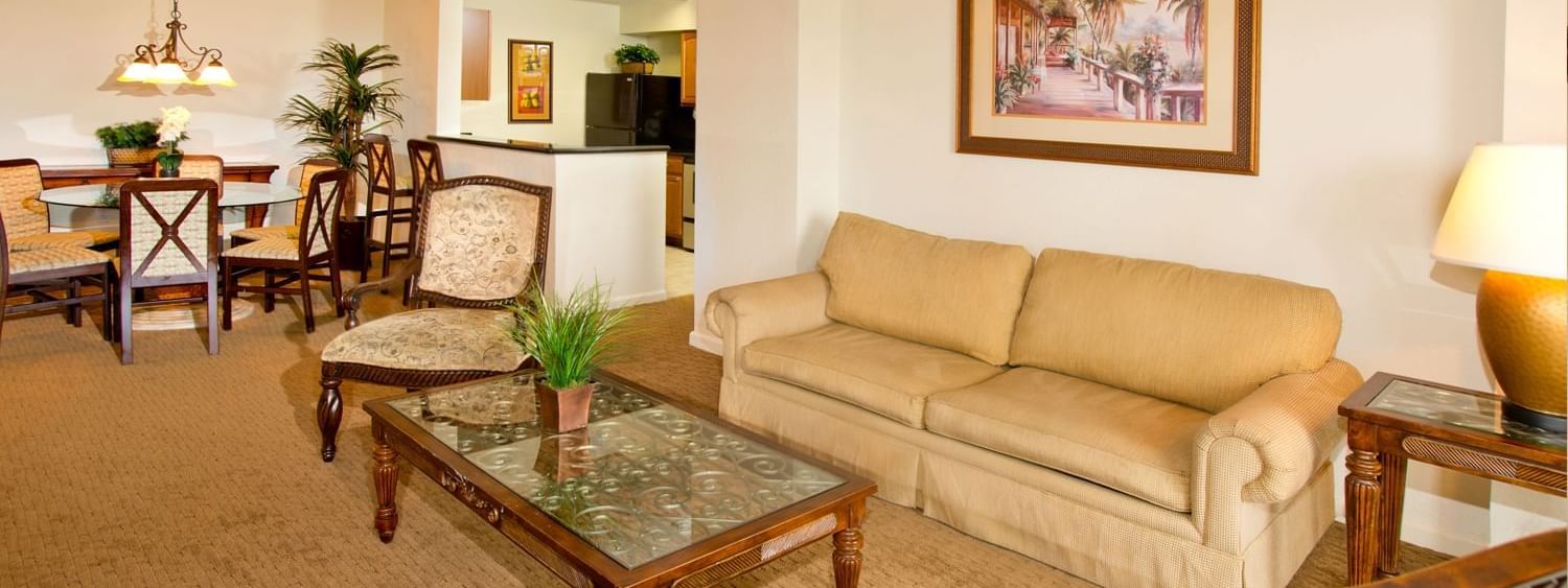 A wide view of a suite's living area with a sofa, coffee table, dining table, and chairs.