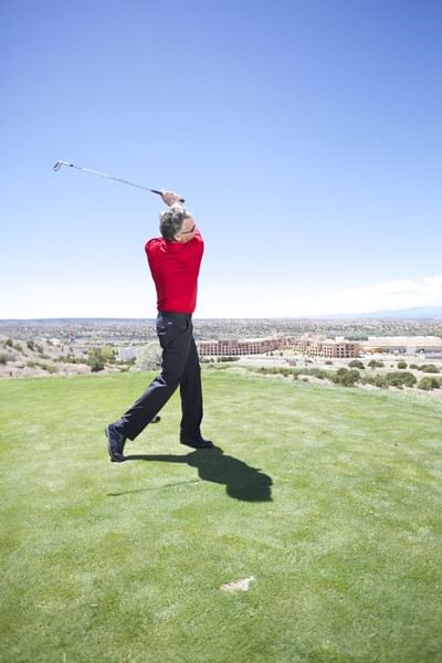Man in a red shirt swinging a golf club at Towa Golf Club course near Hilton Santa Fe Buffalo Thunder