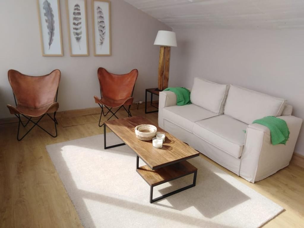 Sala de estar da suíte com sofá branco, duas cadeiras butterfly em couro e mesa de centro de madeira no NOI Indigo Patagonia