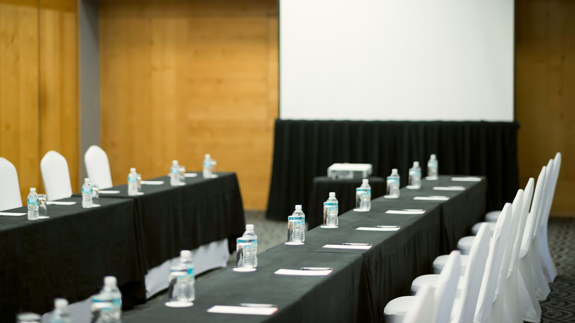 Mexico Venue with black tablecloths, bottled water, and a large white screen at Real Inn Perinorte