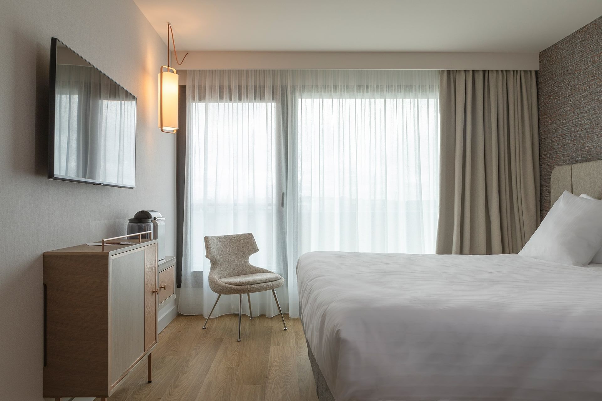 TV et fauteuil face au lit king-size dans une chambre avec plancher en bois à l'Oceania Saint-Malo