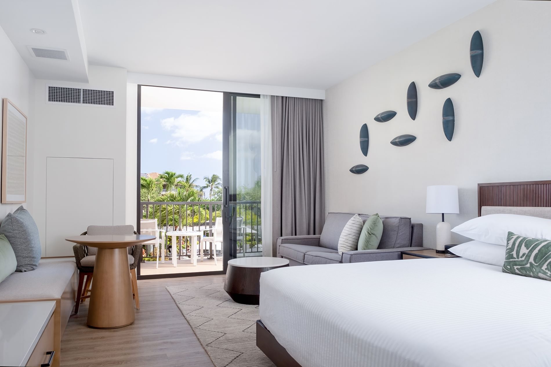 A hotel room with a large bed, sitting area, and sliding glass doors leading to a balcony