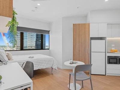 Modern hotel room with bed, desk, microwave, refrigerator, and city view at UniLodge Brisbane City.