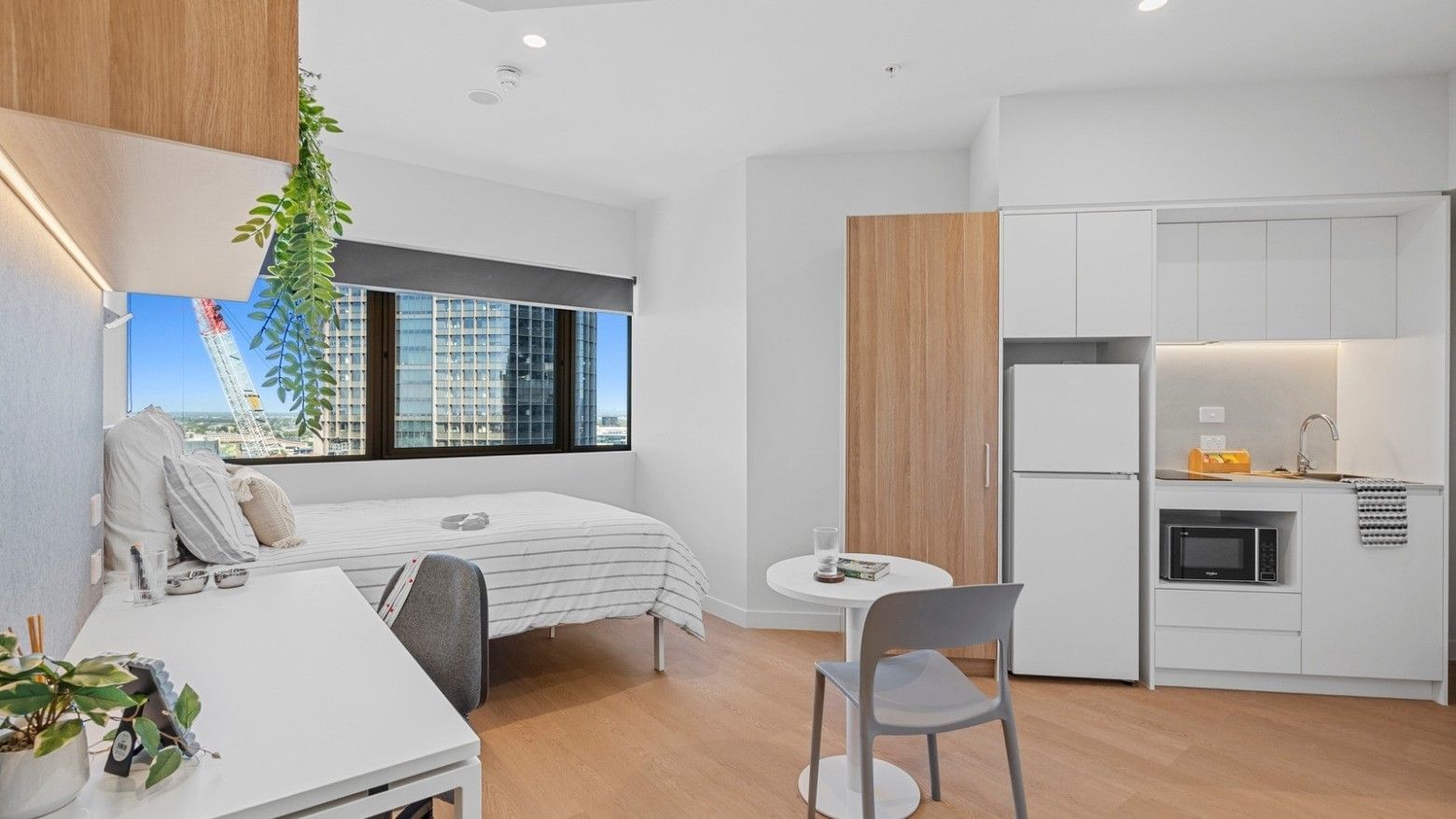 Modern hotel room with bed, desk, microwave, refrigerator, and city view at UniLodge Brisbane City.