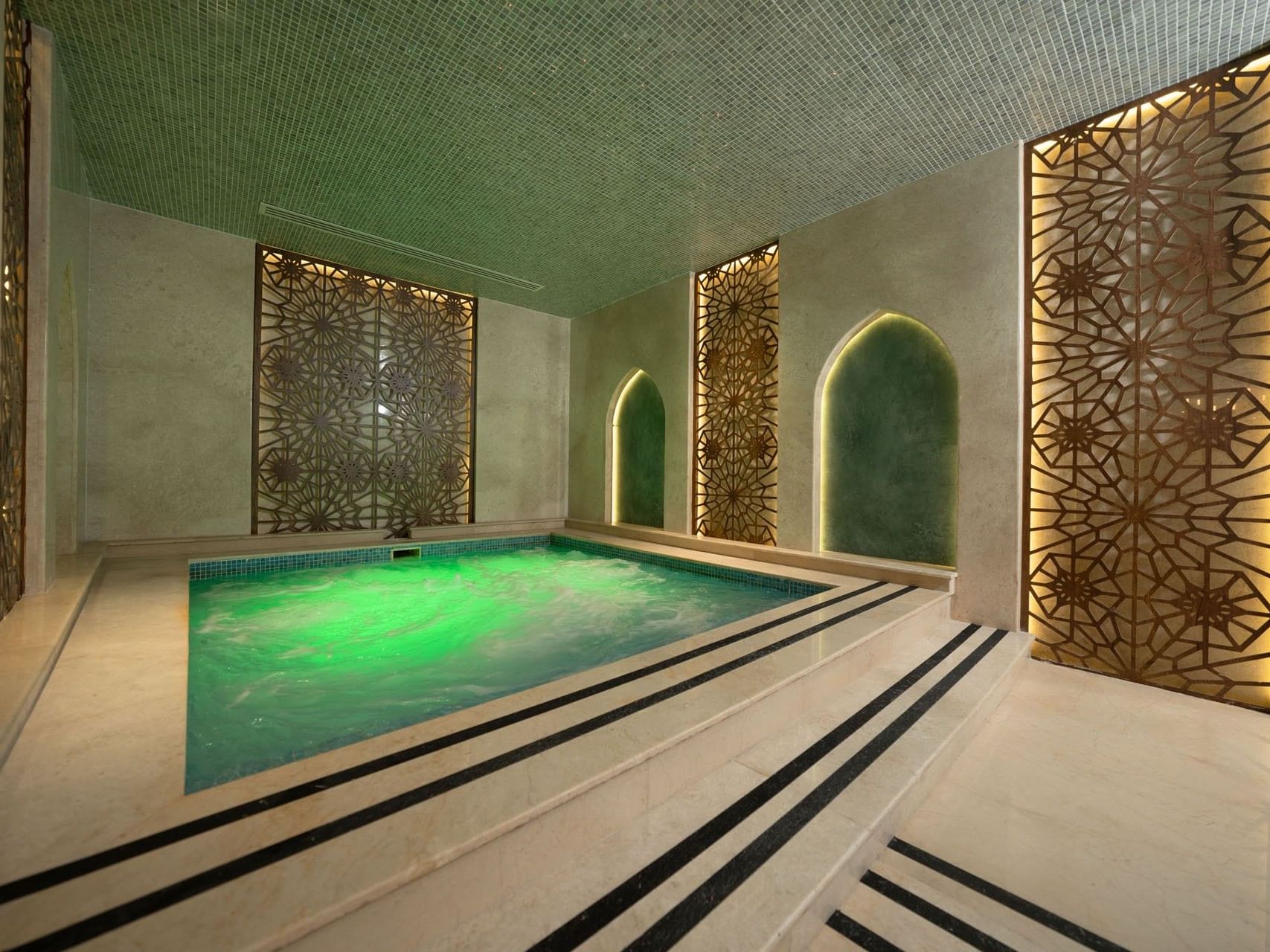 An elegant pool room with green-lit water and ornate walls at World Heart Hotel Baghdad.