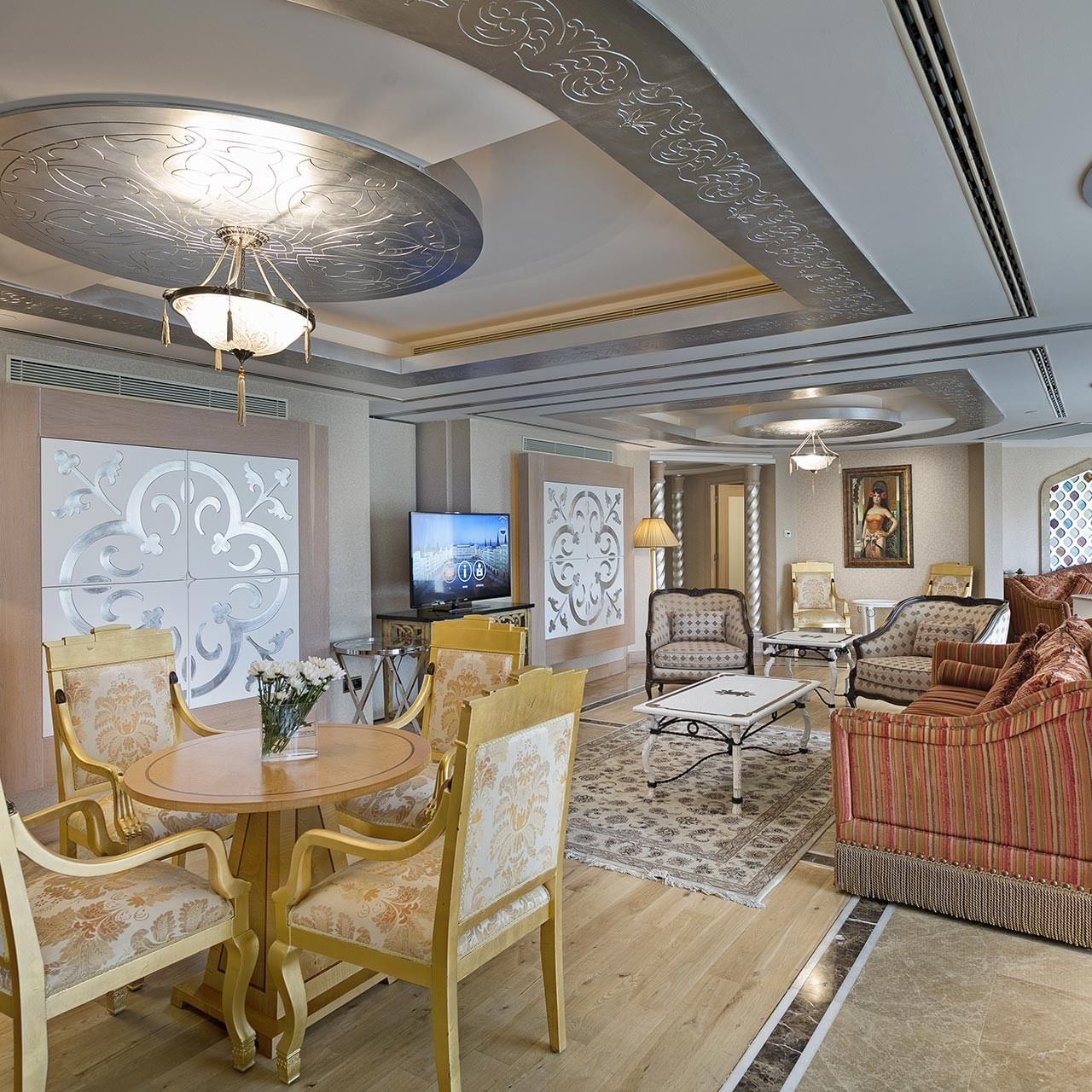 Wohnzimmer im Lake House des Titanic Mardan Palace – mit Möbeln, TV, Kronleuchter und Kunstwerken.
