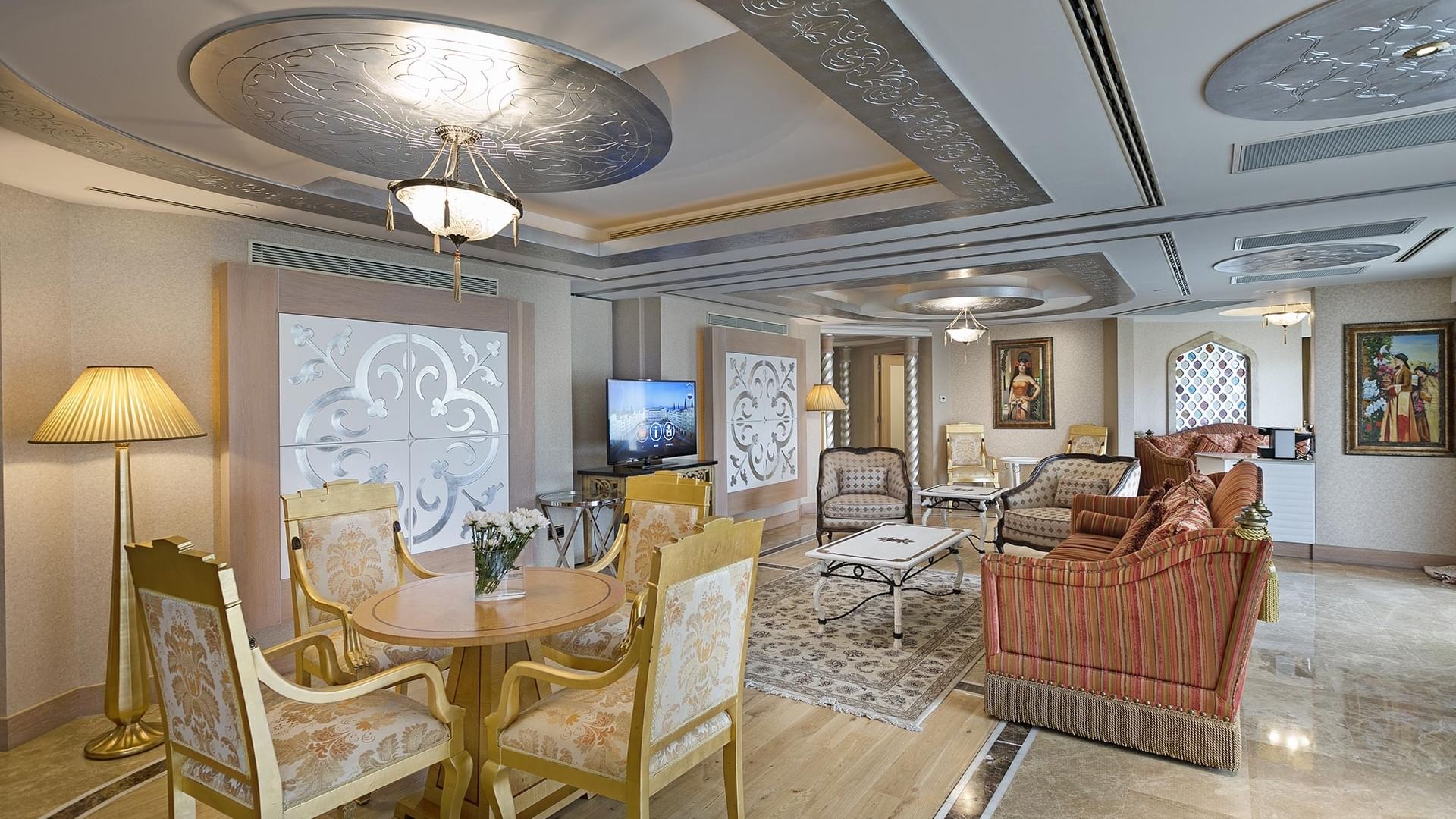 Wohnzimmer im Lake House des Titanic Mardan Palace – mit Möbeln, TV, Kronleuchter und Kunstwerken.