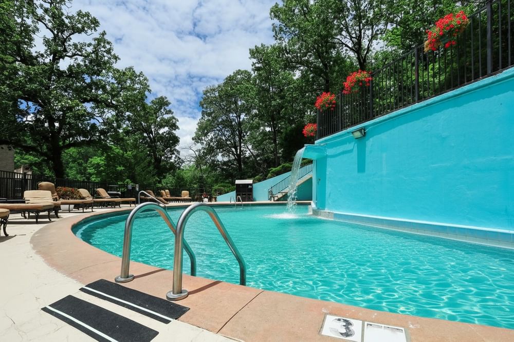 Outdoor pool by a blue wall with a waterfall under a leafy green canopy at Arlington Resort Hotel & Spa