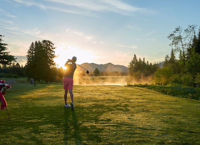 A golfer tees off into the misty sunrise over the course at Lake Placid Club Grandview