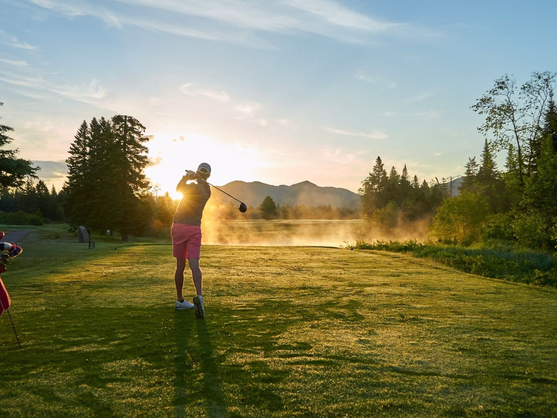 A golfer's silhouetted follow-through on a beautifully lit golf course with mist rising near Lake Placid Club Grandview
