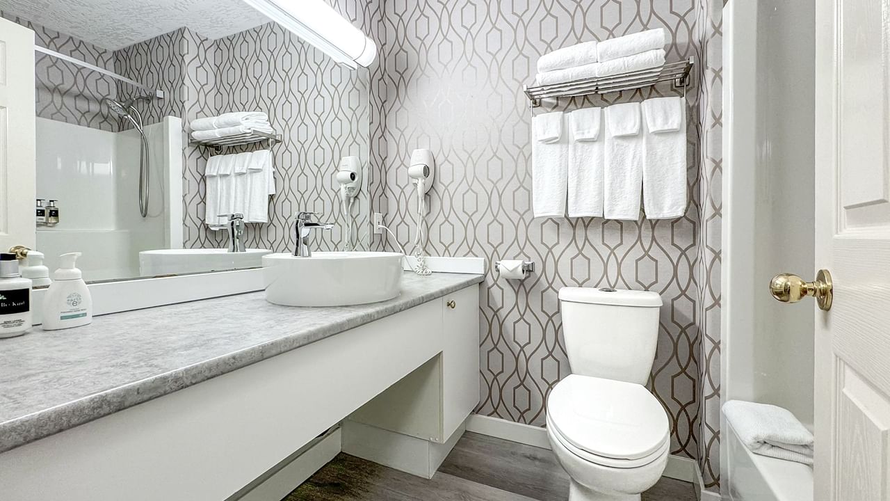 Hotel washroom with toilet, bathtub, sink, towels, and soap