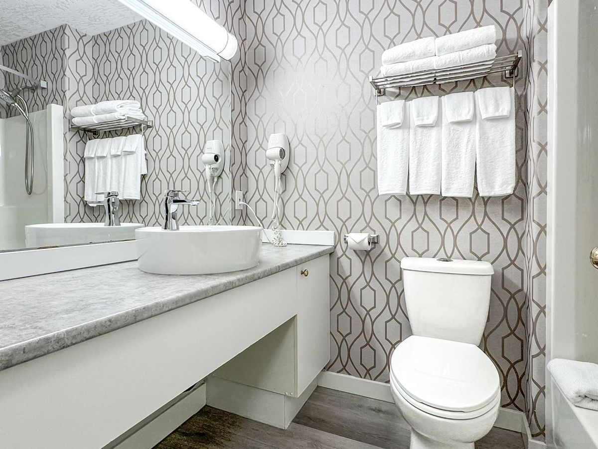 Hotel bathroom with toilet, bathtub, sink, soap, and towels