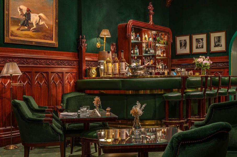 Bar élégant aux murs verts avec boiseries acajou, fauteuils en velours et vitrine de spiritueux à Hotel Westminster Warwick Paris