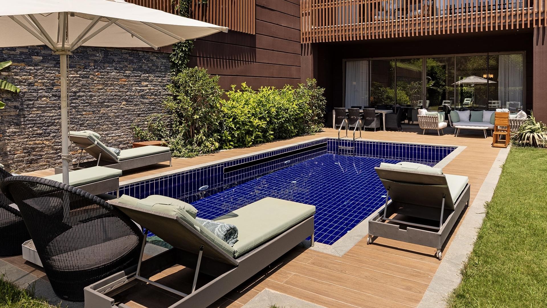 Titanic Luxury Collection Bodrum’daki Exclusive Villa’nın şezlonglu, şemsiyeli ve verandalı havuz kenarı alanı.