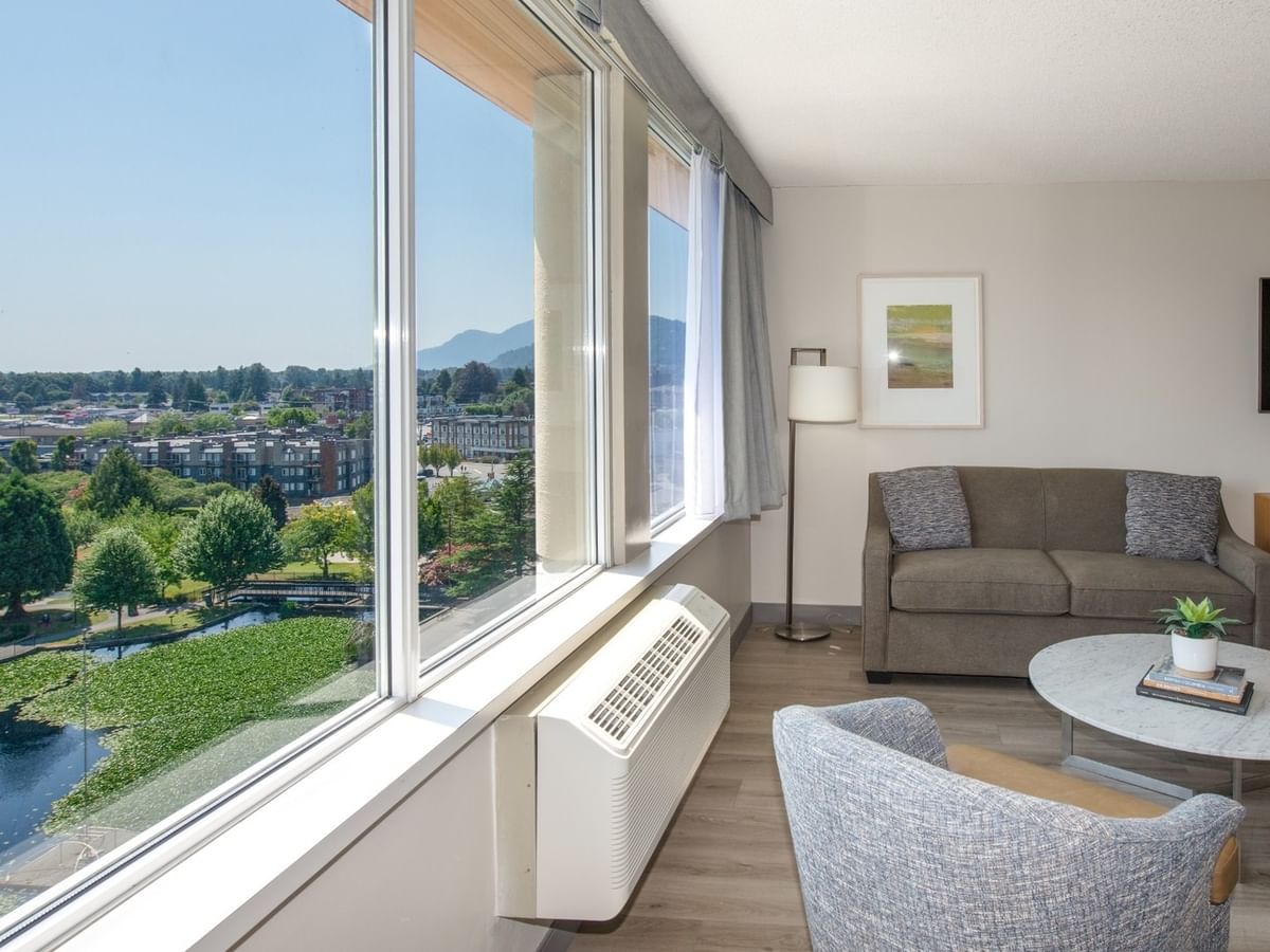 Hotel room with couch, chair, coffee table, TV, and large window with pond view.
