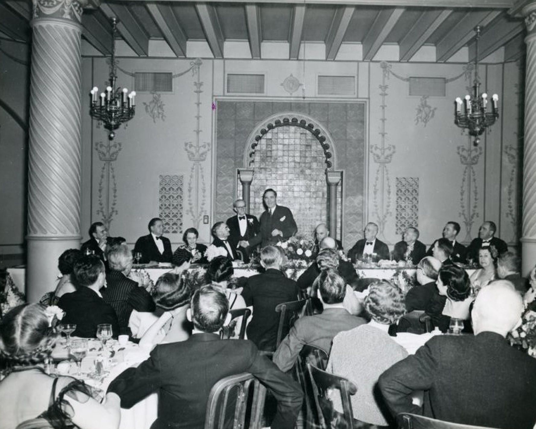 Greyscale picture of guests by formal tables under chandeliers in a historic ballroom at Arlington Resort Hotel & Spa