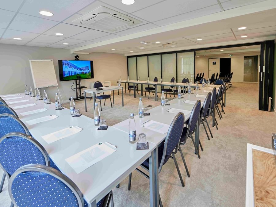 Salle de réunion spacieuse et équipée avec tables, chaises, et écran chez Hôtel La Marébaudière.