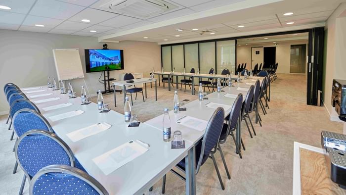 Salle de réunion spacieuse et équipée avec tables, chaises, et écran chez Hôtel La Marébaudière.