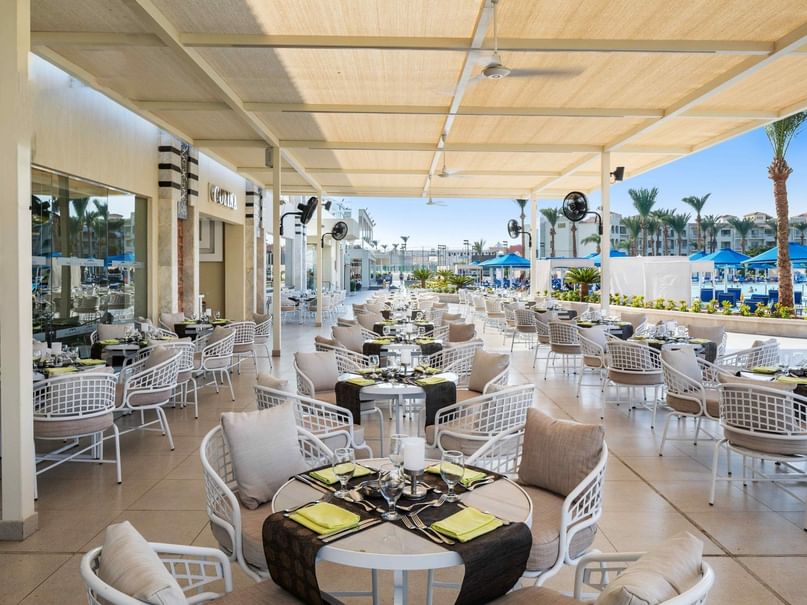 Outdoor dining area with white chairs, black tablecloths, and decorative pillows under a large canopy.
