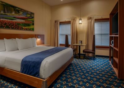 Bed beside a shelving unit and two windows with a small table in the corner of the Suite at Harborside Inn Boston