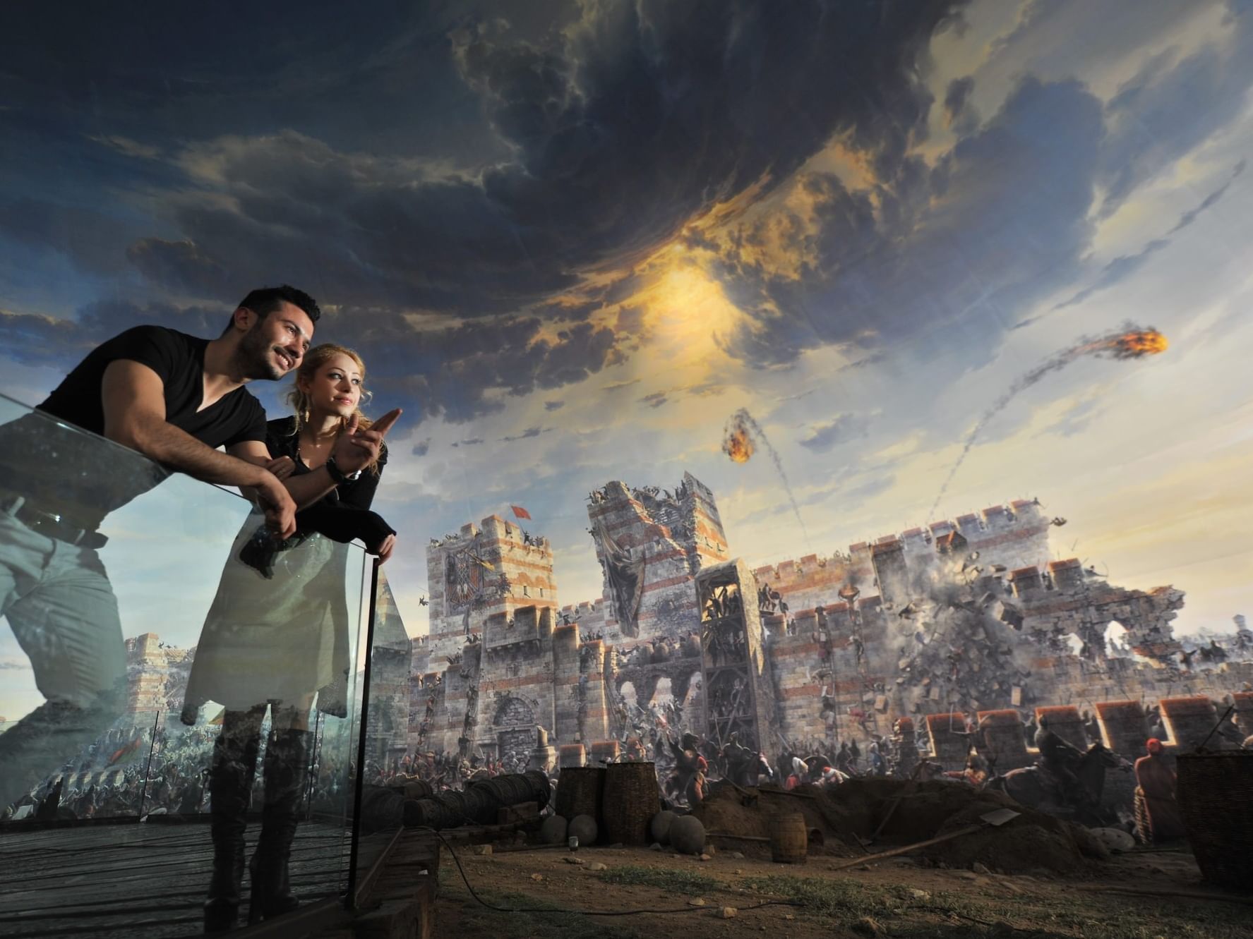 Paar betrachtet eine großformatige historische Schlachtszene mit Festung und Himmel voller Wolken.