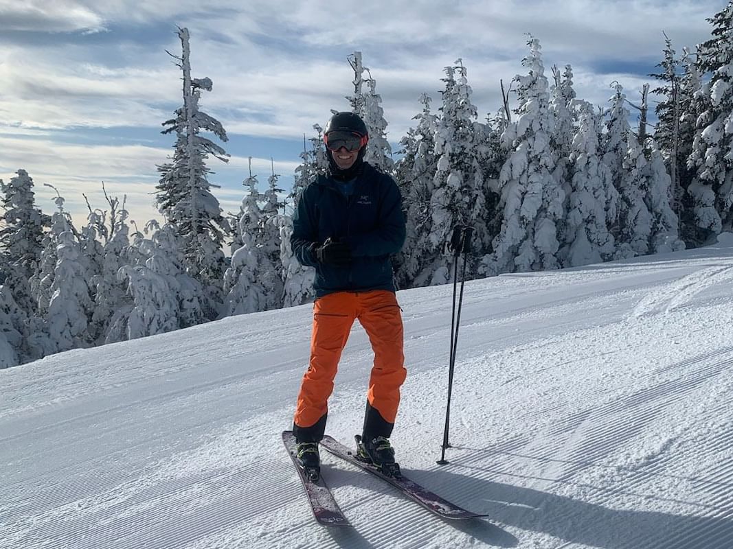 Man standing on a freshly groomed ski slope, with snow-covered trees near High Peaks Resort