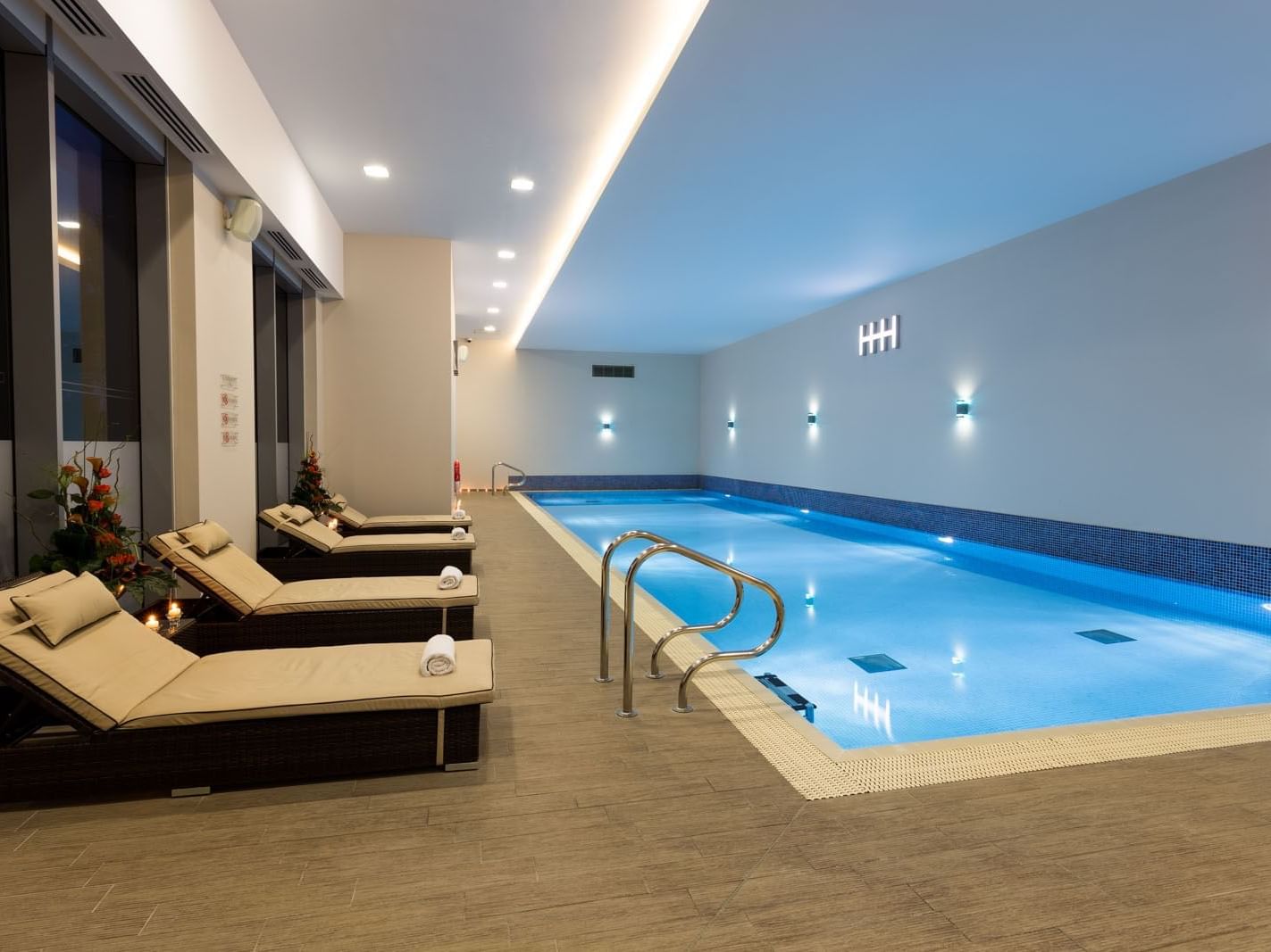 Lounge chairs placed beside a heated indoor pool, glowing under soft lights at Heston Hyde Hotel