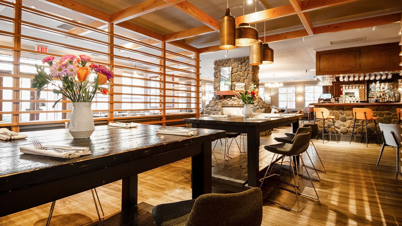A dining area with wooden tables, chairs, flower vases, and a bar counter.