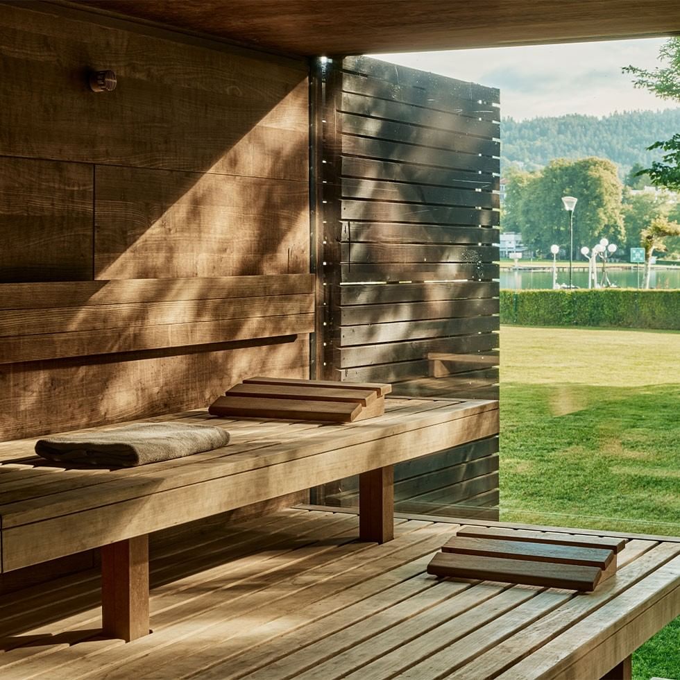 Hölzerne Sauna mit Sicht auf einen Park und einen See, umgeben von Bäumen und einem Berg.