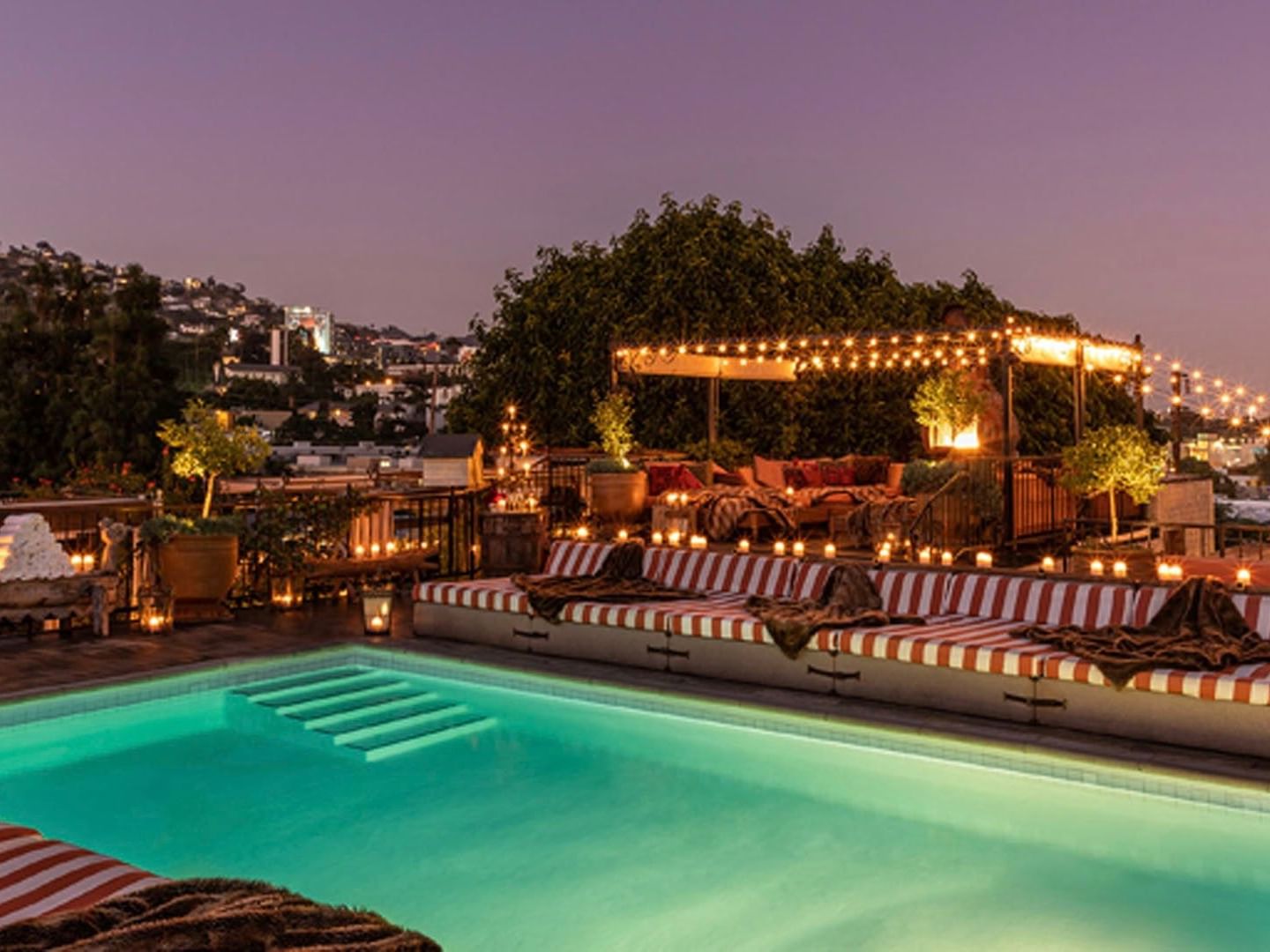 Pool Deck with swimming pool illuminated by string lights with striped loungers and city views at Petit Ermitage