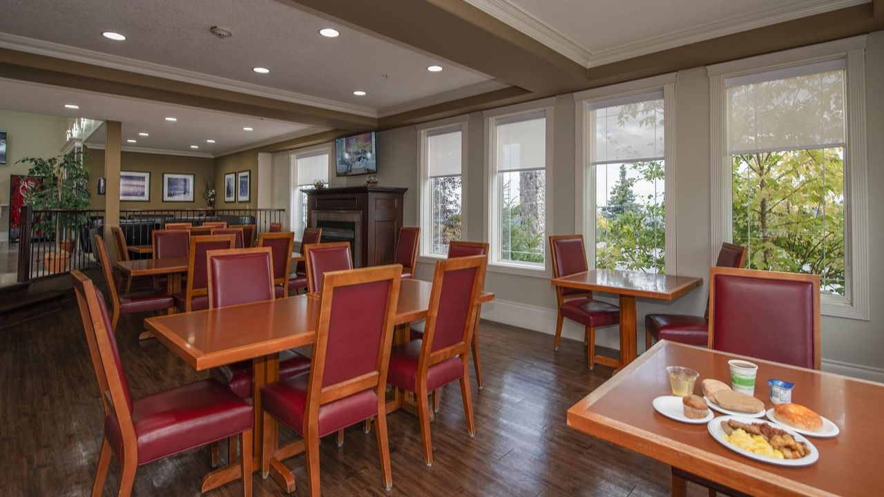 Bright dining area with wooden tables, red leather chairs, and large windows overlooking trees at Coast Edson Hotel.