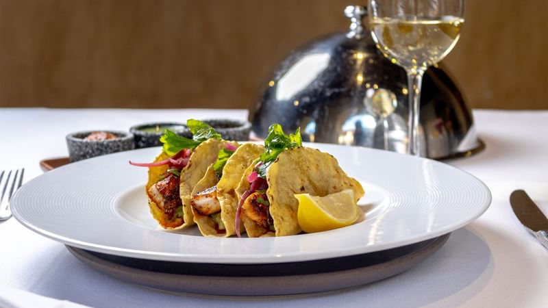 Tres tacos de pescado frescos en plato blanco con limón y vino blanco en Quinta Real Oaxaca