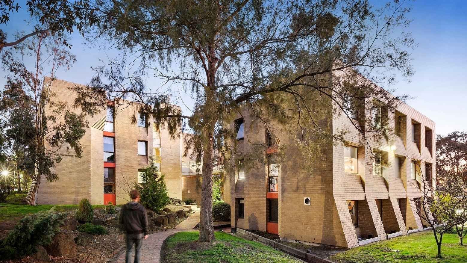 Person walking on pathway by La Trobe University - Chisholm College building.