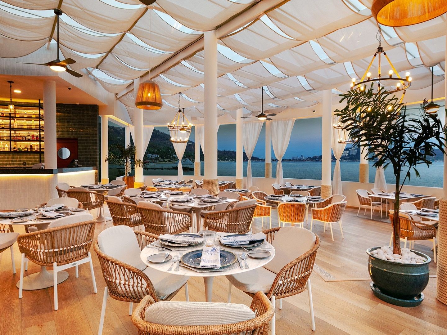 La Vela waterfront restaurant at dusk with wicker chairs and draped ceilings in Camino Real Acapulco Diamante