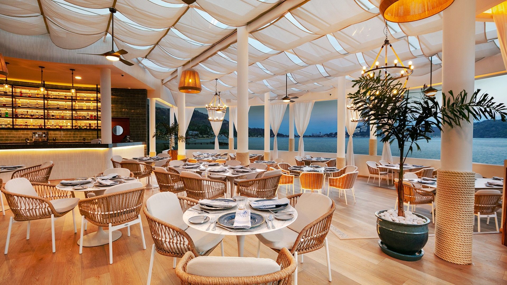 La Vela waterfront restaurant at dusk with wicker chairs and draped ceilings in Camino Real Acapulco Diamante