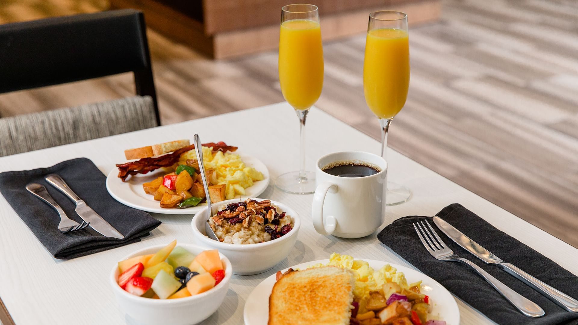 A breakfast table with plates of food, glasses of orange juice, and a cup of coffee.