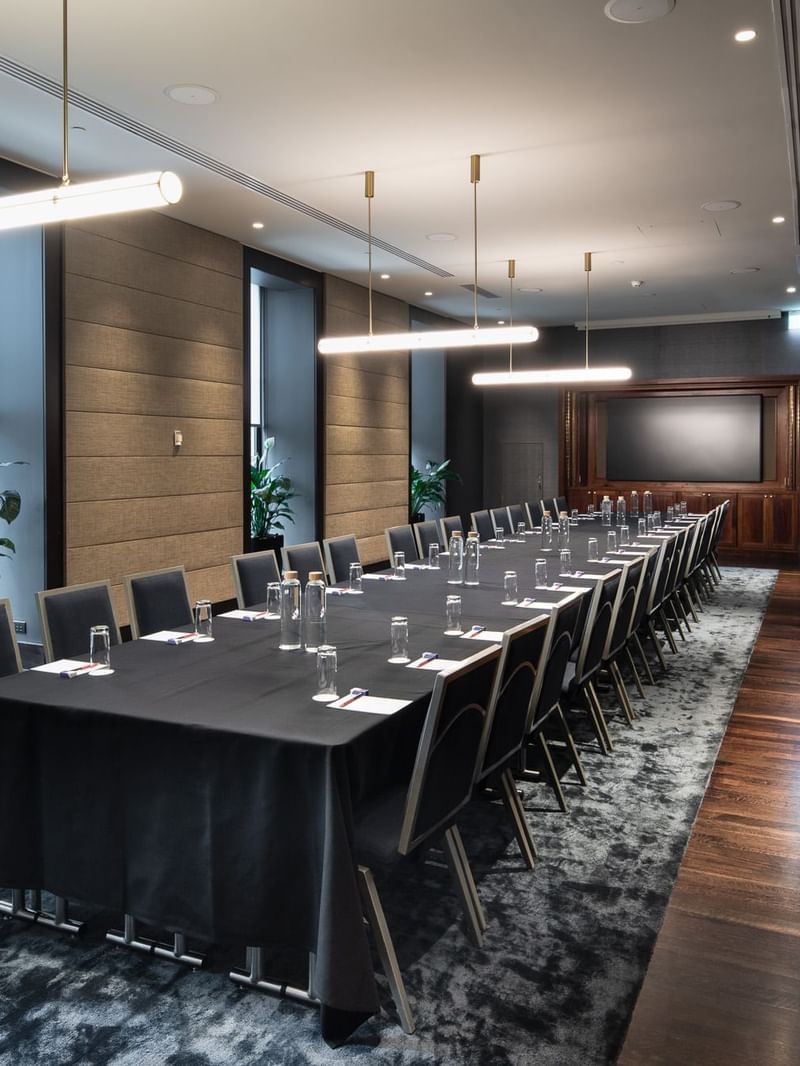 Modern conference room with long table, black tablecloth, chairs, water bottles, plants, and a large window.