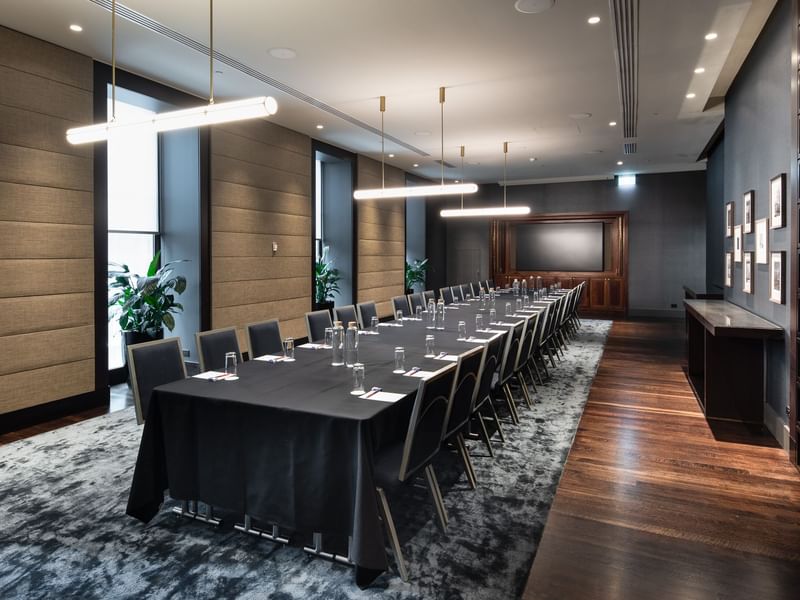 Modern conference room with long table, black tablecloth, chairs, water bottles, plants, and a large window.