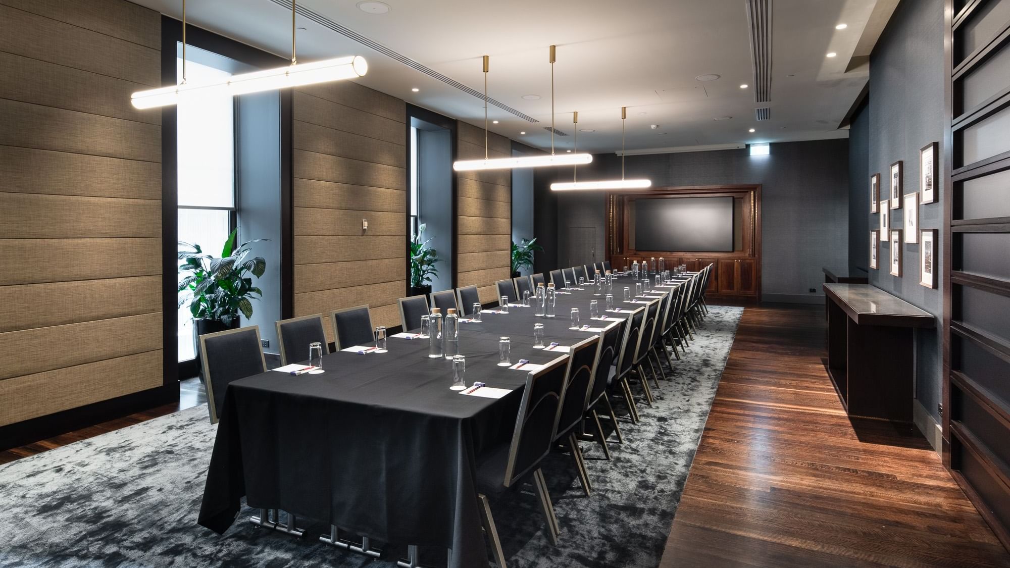 Modern conference room with long table, black tablecloth, chairs, water bottles, plants, and a large window.