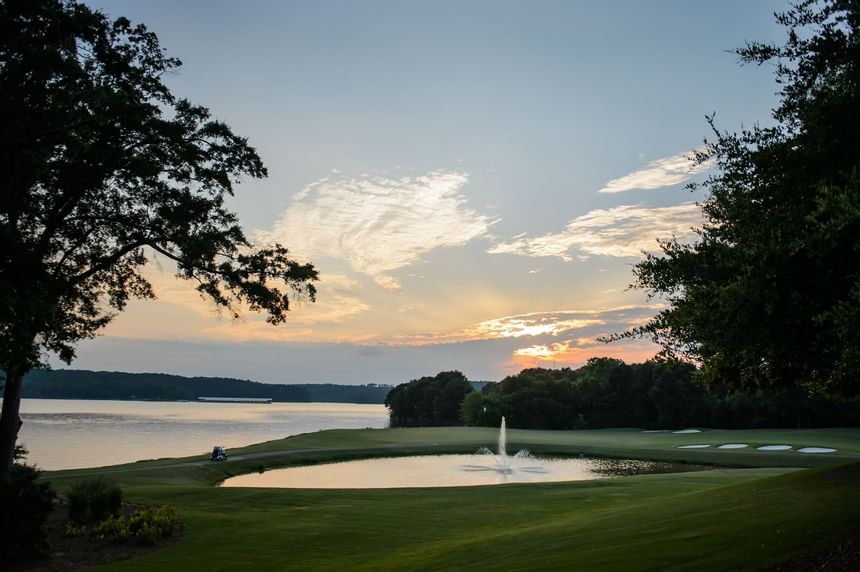 Sunset sky over calm lake waters with a fountain pond on a green golf course at Clemson University Conference Center & Inn