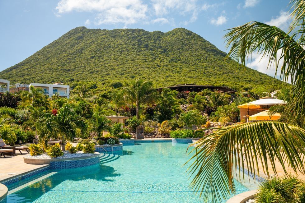 Tropisch zwembad met palmbomen, bergzicht en ligstoelen bij Golden Rock Resort