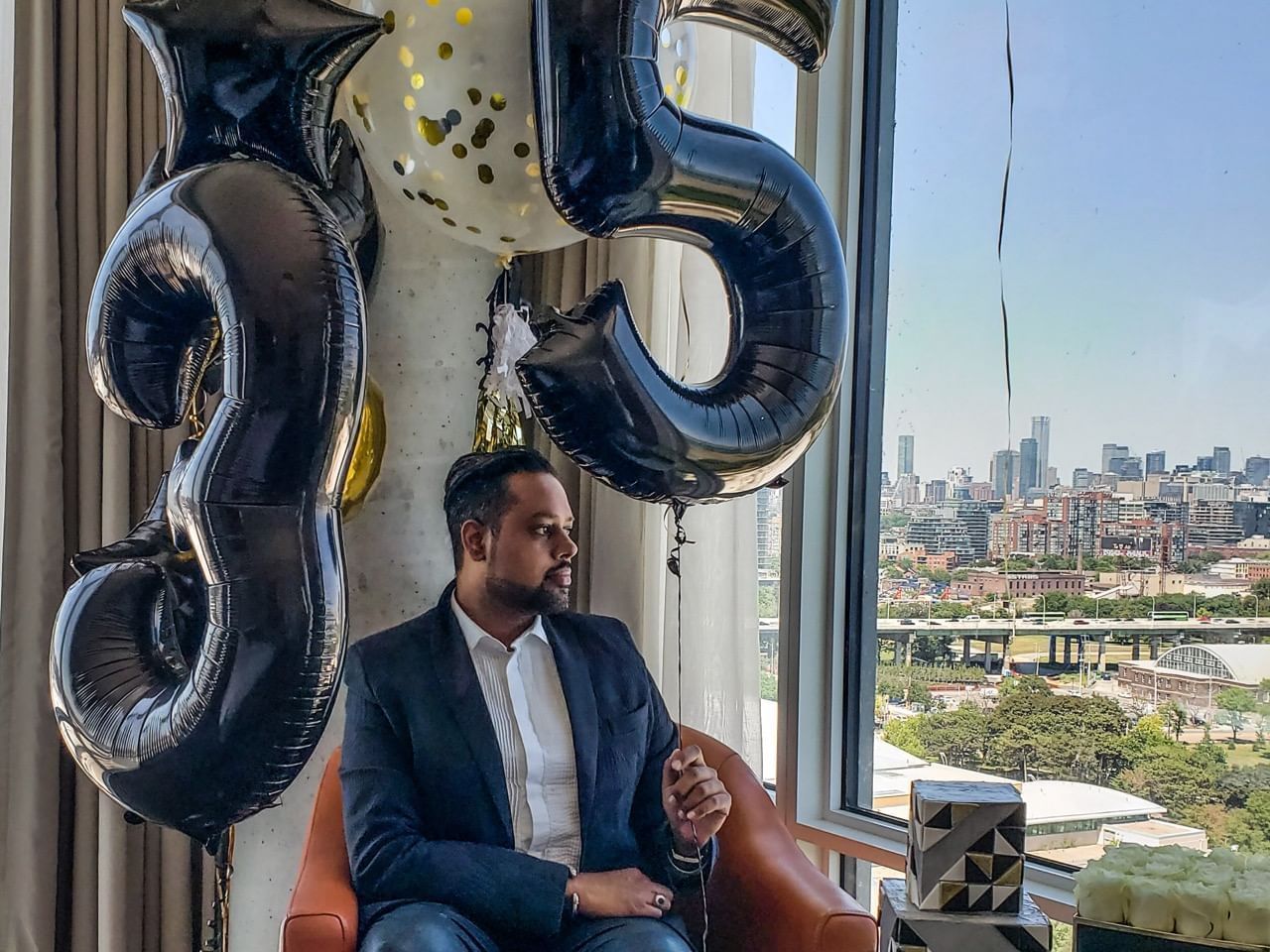 Person seated by a window with a city view and balloons featuring, Birthday Celebration Package at Hotel X Toronto