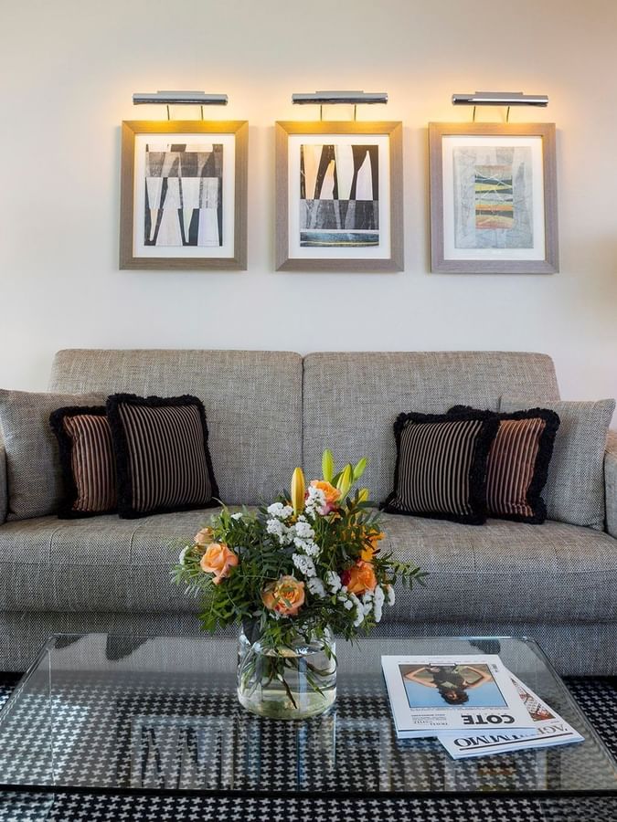 Grey sofa by glass tables under glowing art surrounding a patterned rug in Penthouse Terrace Suite at Warwick Geneva
