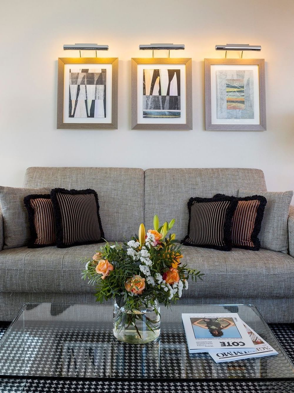 Grey sofa by glass tables under glowing art surrounding a patterned rug in Penthouse Terrace Suite at Warwick Geneva