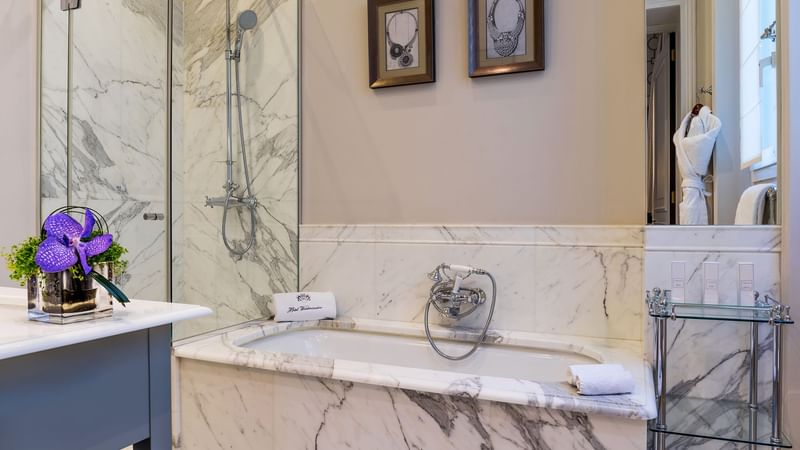 Bathroom with a marble bathtub, sleek shower, and adorning plant in Deluxe Parisian suite at Hôtel Westminster - Paris