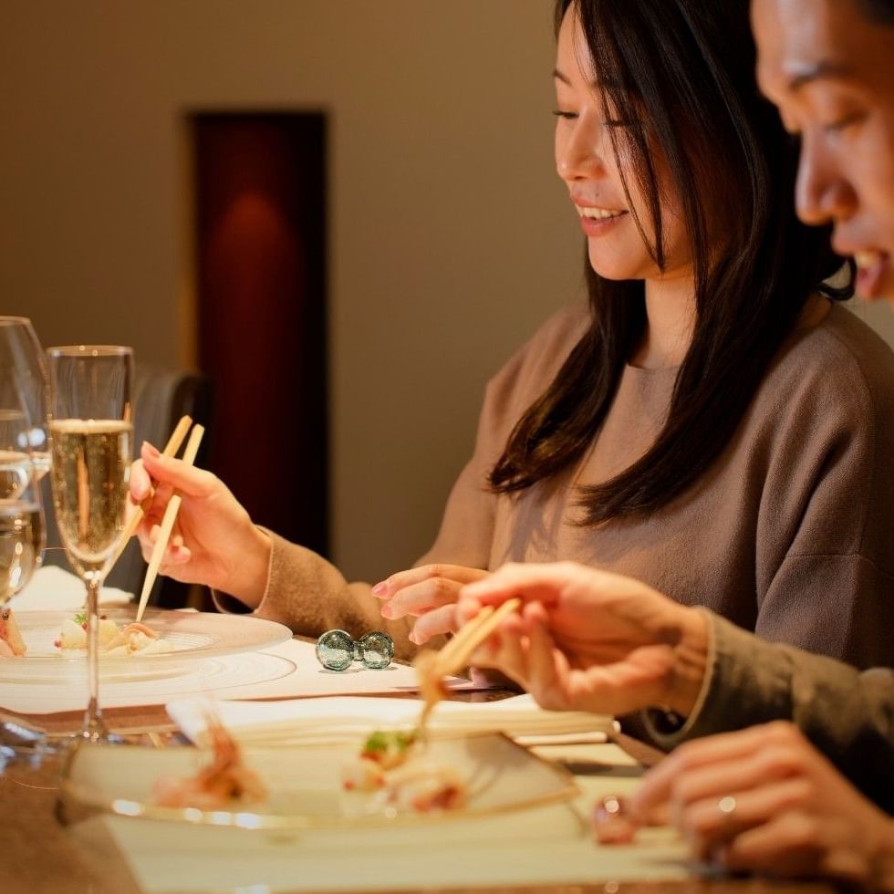 Couple enjoys fine dining with chopsticks, plated dishes, and sparkling drinks at Cocoro Restaurant in Grand Park Otaru