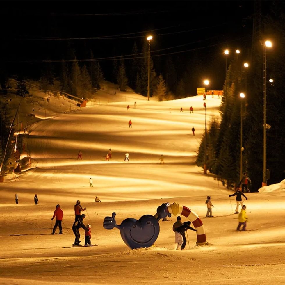 Nighttime ski event with skiers and a large blue snow sculpture.
