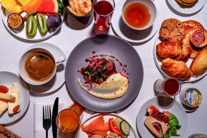 Plates of steak and eggs by cups of coffee and fresh fruit on a white table in Sunday Brunch at Warwick Paris Champs Elysées