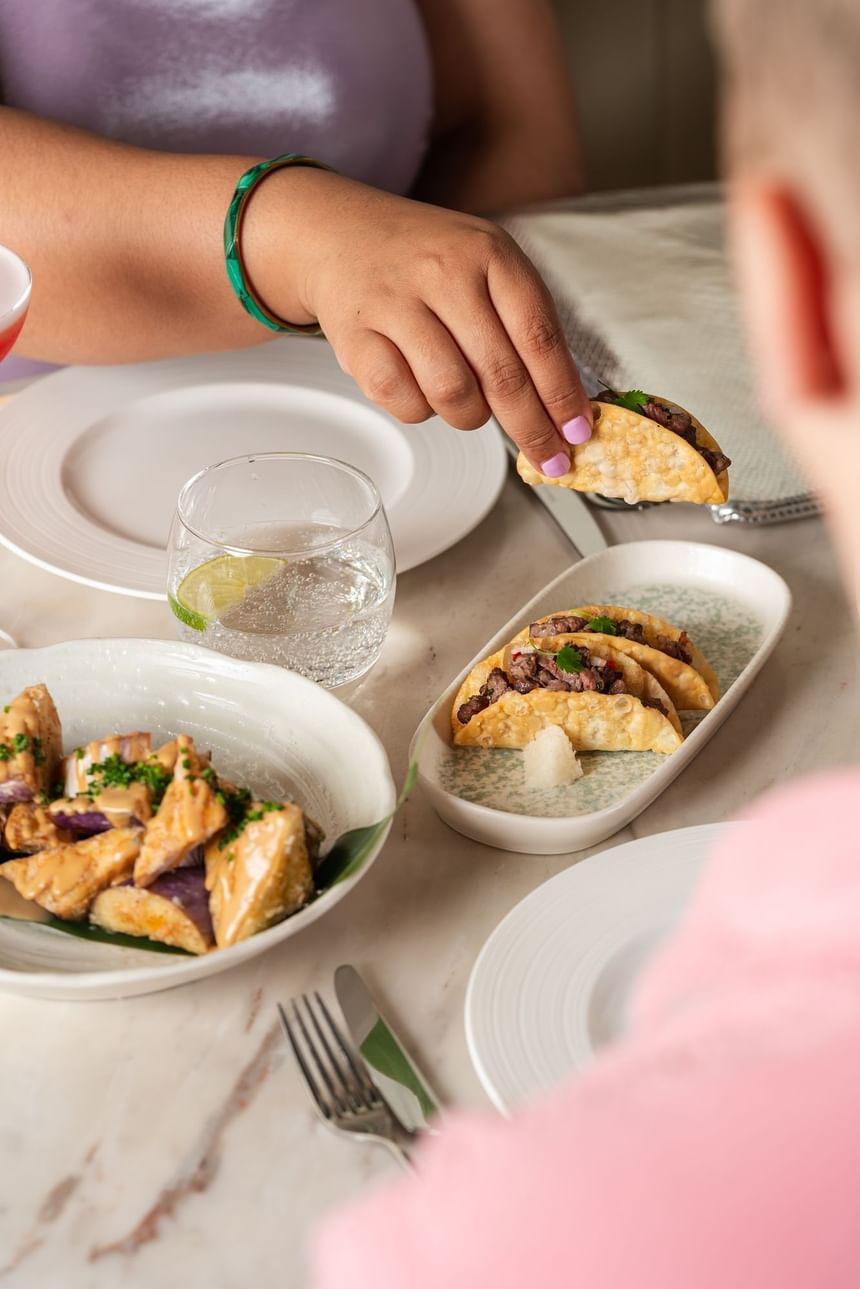  Hand reaching for a taco with a plate of colorful salmon & a glass of sparkling water at Peter Street Kitchen