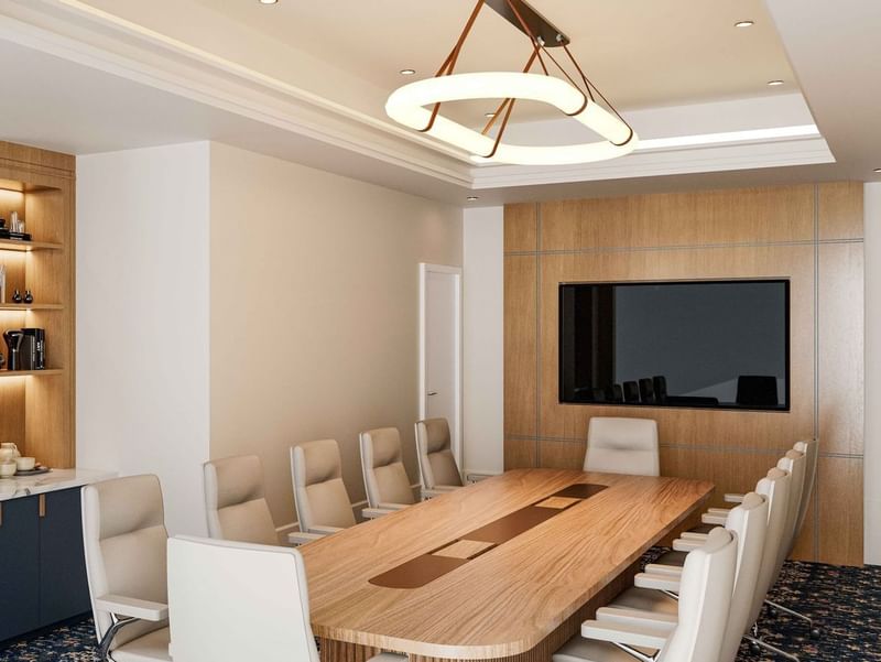Modern boardroom at El Prado Hotel, with a long wooden table, comfortable chairs, and a large screen
